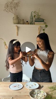 two young women standing in front of a table with plates and bowls on the table