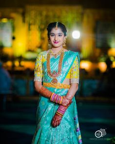 a woman in a green and yellow sari holding her hand on her hip, with the lights behind her