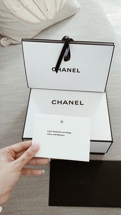 a person holding up a chanel card in front of a box on a couch