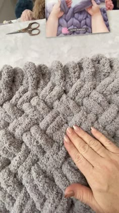 a hand is holding the edge of a crocheted blanket next to a pair of scissors