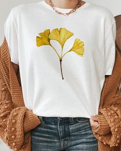 T-shirt featuring a botanical illustration of a fall Gingko leaf. Fall in love with our autumn leaf shirt you won't find anywhere else. Printed on a white cotton t-shirt, made from durable lightweight cotton. Unisex fit - boxy and long. How it's made: * All prints are original watercolor designs hand-painted by a botanical artist. * Ethically made 100% cotton t-shirts that are made to last. * T-shirts are printed and shipped by my printing partner in the US, Canada, or Europe. * By buying from this shop you are directly supporting a woman-owned small business, created out of love for plants to educate, inspire and keep us connected to the natural world. About the artist: This Shop is an extension of my botanical illustration studio, where I create hand-painted watercolor art for internatio Casual Fall Shirt With Plant Print, Yellow Graphic Print Shirt For Fall, Casual Fall Tops With Plant Print, White Tops With Plant Print For Fall, Fall Short Sleeve Shirt With Plants Print, Casual T-shirt With Plants Print For Fall, Casual Plants Print T-shirt For Fall, White T-shirt With Plant Print For Fall, Casual Fall T-shirt With Plant Print