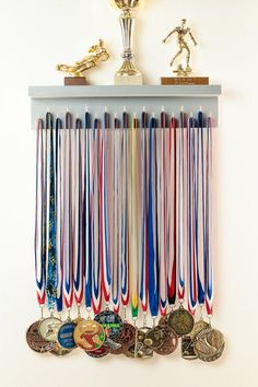 a wall mounted medal rack with medals and trophy cups on it's sides in front of a white wall