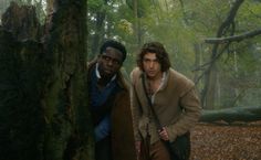 two men standing next to each other in the woods