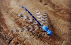 two small blue and white feathers on a piece of wood with one feather stuck to it's tip