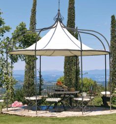 an outdoor gazebo with tables and chairs in the grass next to some tall trees