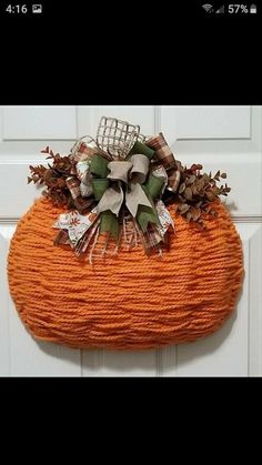 an orange knitted pumpkin hanging on the front door with a bow and plaid ribbon