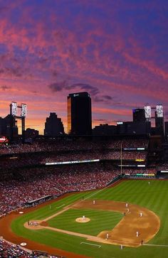 a baseball stadium filled with lots of people watching the sun go down in the distance