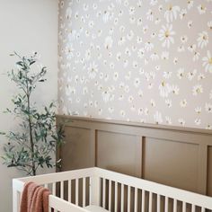 a white crib in front of a wall with flowers on it and a potted plant next to the crib