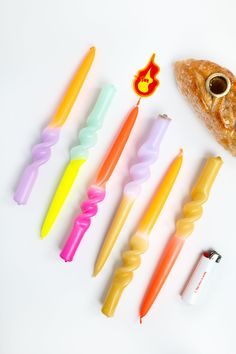 several different colored candles are lined up next to a piece of bread on a white surface