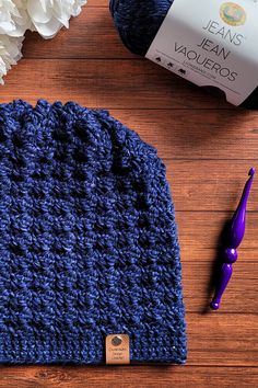 a blue crocheted hat sitting on top of a wooden table next to a bottle of yarn