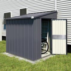 an outhouse with the door open on grass next to a building and a car