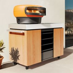 an oven sitting on top of a wooden cabinet next to a potted plant in a room