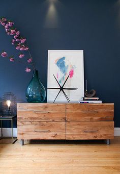 a wooden dresser sitting next to a blue wall with flowers on top of it in a room