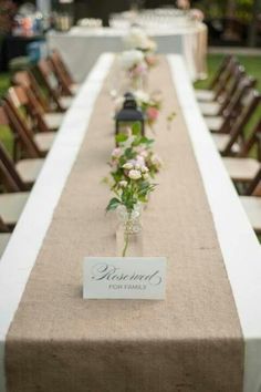 a long table is set up with flowers in vases and place cards on it