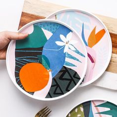 a person holding a plate with colorful designs on it next to other plates and utensils