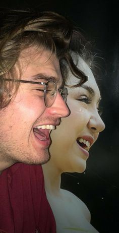 a man with glasses is laughing next to a woman's face in front of a movie poster