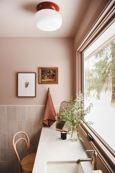 a bathroom with pink walls and white counter top next to a large window that has a painting on the wall