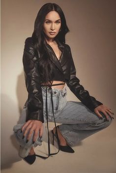 a woman in black jacket and jeans sitting on the ground with her hand on her hip