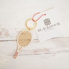 a wooden tennis racket keychain with a black door studio logo on it