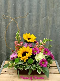 a wooden table topped with a vase filled with lots of different colored flowers and greenery