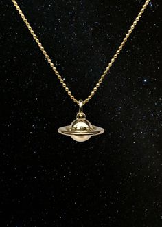 a gold necklace with a saturn pendant hanging from it's side on a black background