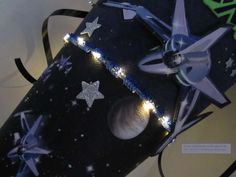 an origami box with stars and planets on it, next to a string of lights