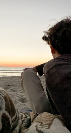 a man sitting on top of a sandy beach next to the ocean at sunset or dawn