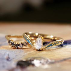 two wedding rings sitting on top of a wooden table next to each other with different colored stones