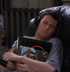 a man laying in a chair with headphones on and holding a book over his face