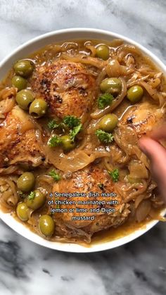 a white bowl filled with chicken and olives on top of a marble countertop