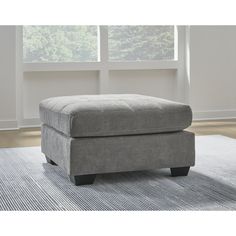 a gray foot stool sitting on top of a rug in front of a large window