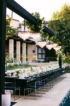 an outdoor dining area with long tables and chandeliers hanging from the ceiling, surrounded by greenery