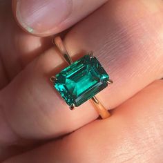 a woman's hand holding a ring with an emerald stone in the middle and a gold band around it