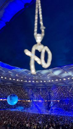 a large group of people in a stadium with lights on the ceiling and an object hanging from the ceiling