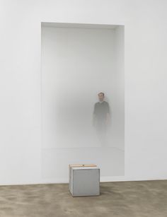 a man standing in front of a white wall with a square object on the floor