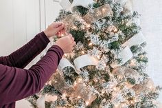 a person decorating a christmas tree with white and silver ribbons