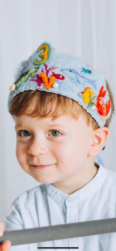 a young boy wearing a blue hat with fish on it and holding a metal object in front of his face