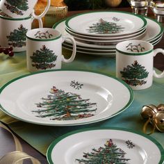 a table topped with plates and cups covered in christmas tree designs on green placemats