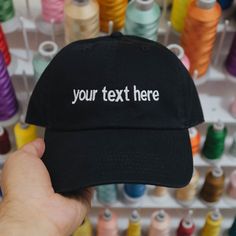 a person holding up a black hat with the words your text here embroidered on it