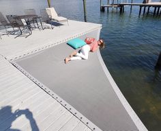 a woman laying on top of a dock next to the water with a pillow in her hand