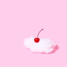 a cherry sitting on top of a cloud with a pink wall in the back ground