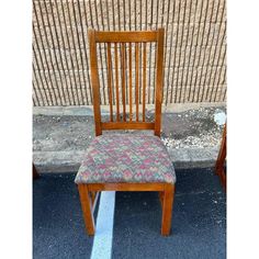 two wooden chairs sitting next to each other in front of a brick wall on the sidewalk