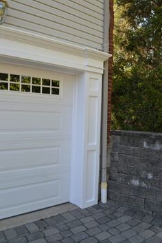 a white garage door is open in front of a brick wall