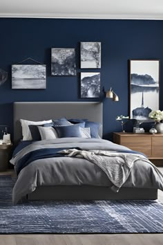 a bedroom with blue walls and grey bedding, pictures on the wall above it