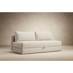 a white couch sitting on top of a floor next to a beige wall with two pillows