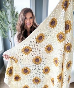 a woman holding up a crocheted blanket with sunflowers on it and smiling at the camera