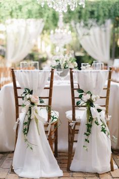 two wooden chairs with white sashes and flowers on them are set up for an outdoor wedding