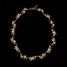 a gold necklace with pearls and leaves on it, against a black background - stock photo