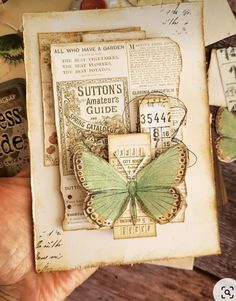 a hand holding up a card with a green butterfly on it and some old papers