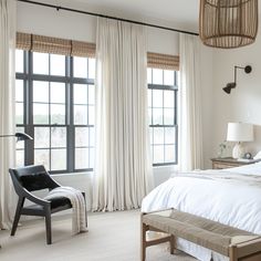 a bedroom with large windows and white linens on the bed, along with a black chair